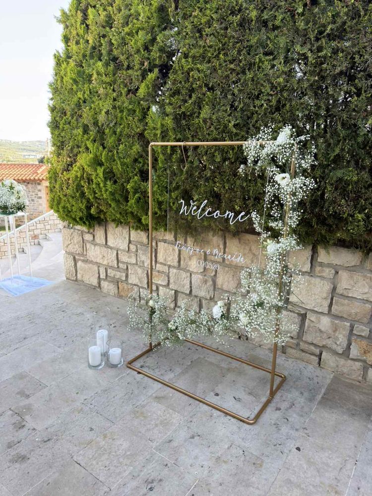 Χρυσό welcome frame γάμου με γυψοφίλη σε πέτρινο τοίχο